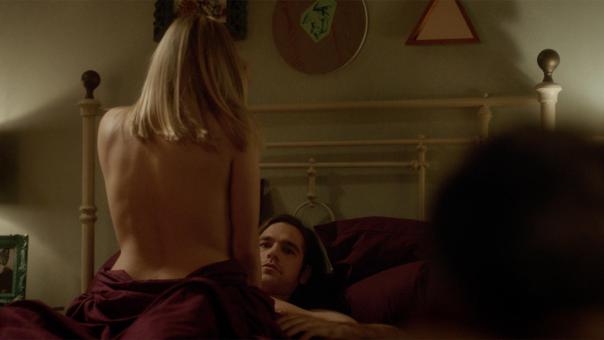 Alice with her back turned, sitting on top of a prone Quentin in bed