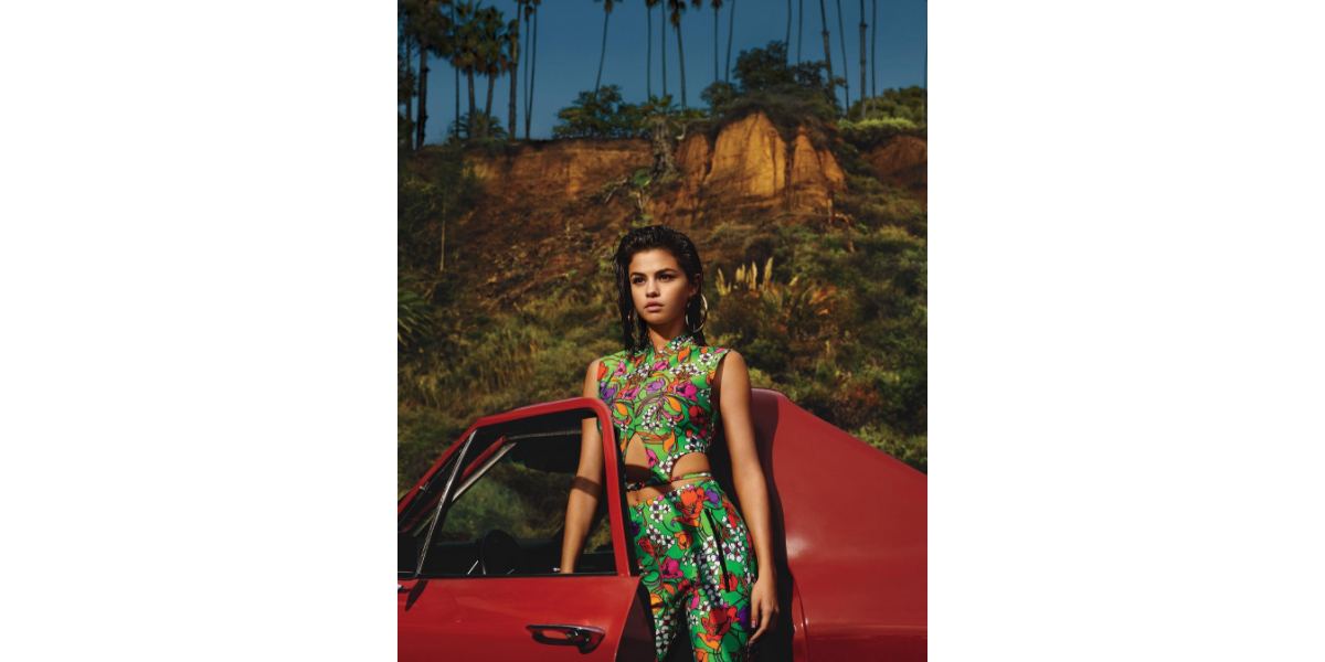 Selena Gomez wears a multicolor jumpsuit as she stands in front of a red car in a shot from her Vogue Magazine spread.