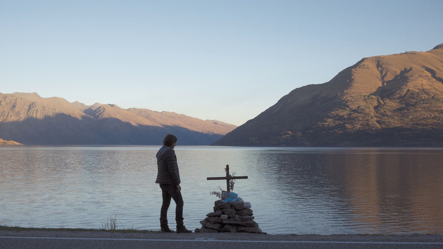 Robin Griffin stands in front of a memorial overlooking a gorgeous lake and mountains in a scene from 'Top of the Lake.'