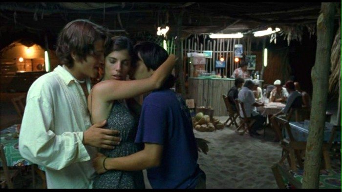 Three young people embrace in a hug, in a dingy, poorly lit room
