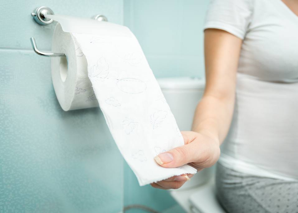 Closeup photo of woman sitting on toilet and using toilet paper