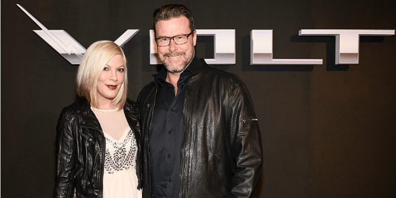 Tori Spelling and Dean McDermott pose together in front of a Volt sign.