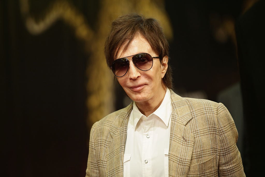 Michael Cimino wearing a tan jacket and sunglasses, smiling for the camera