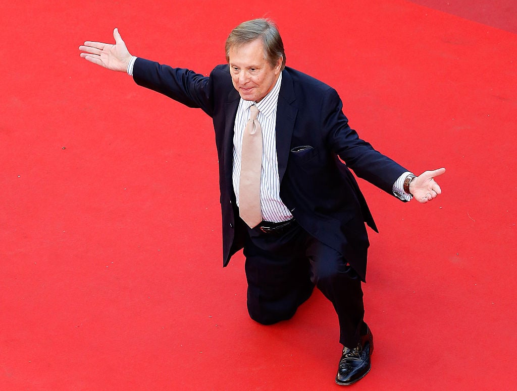 William Friedkin down on one knee on the red carpet, with both arms extended out