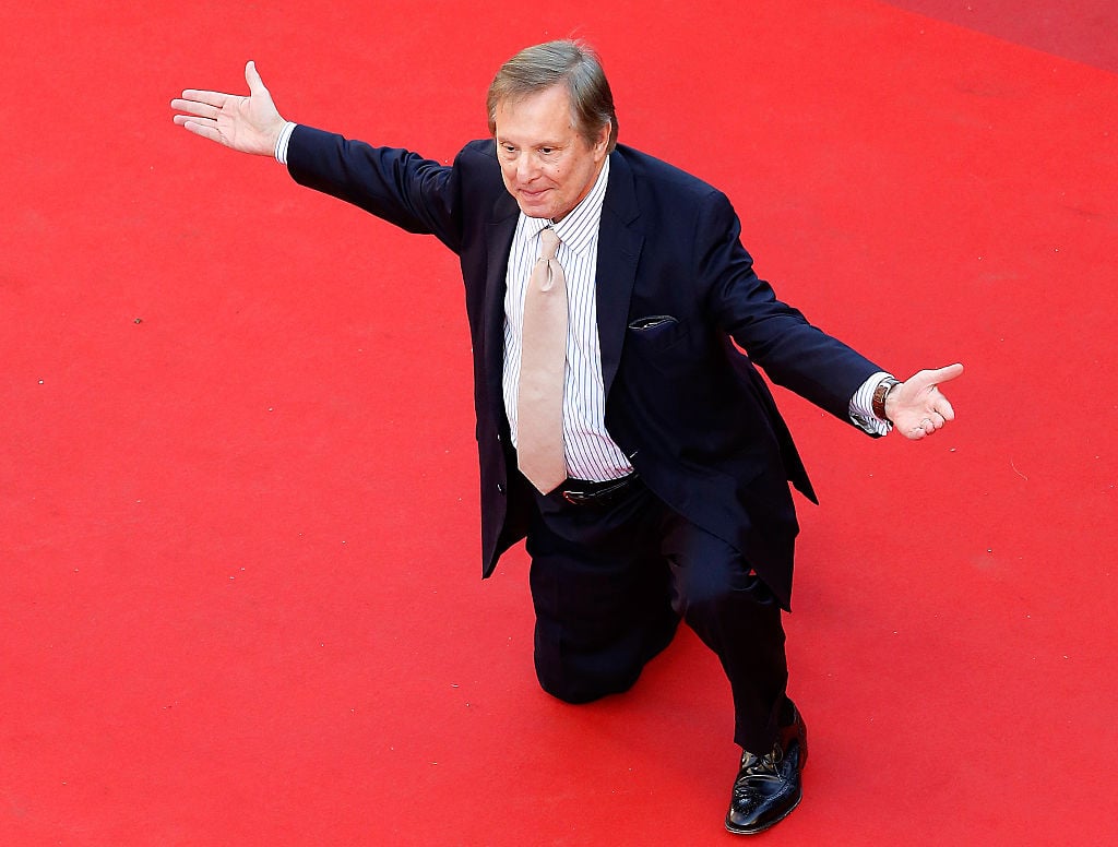 William Friedkin down on one knee on the red carpet, with both arms extended out