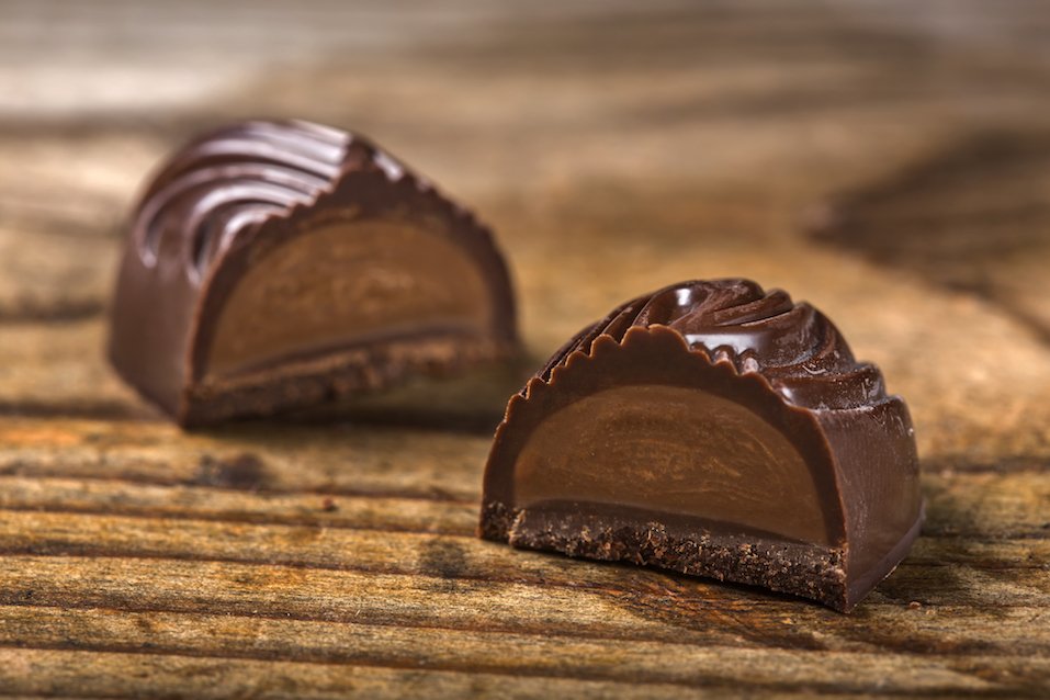 One dark chocolate candy cut in half over wooden background
