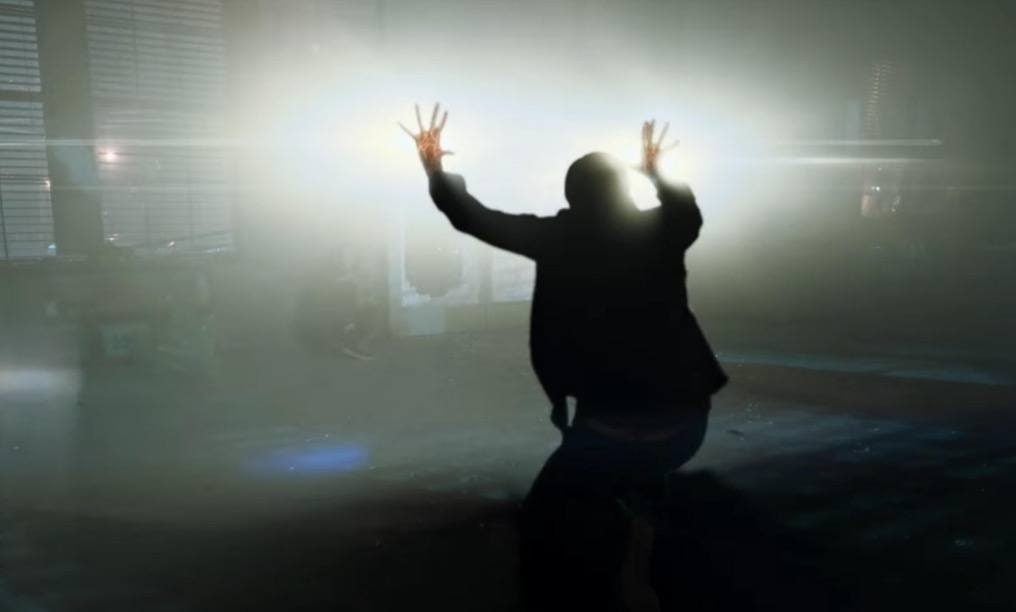 A man with light coming from both hands hold both up with his back turned to the camera