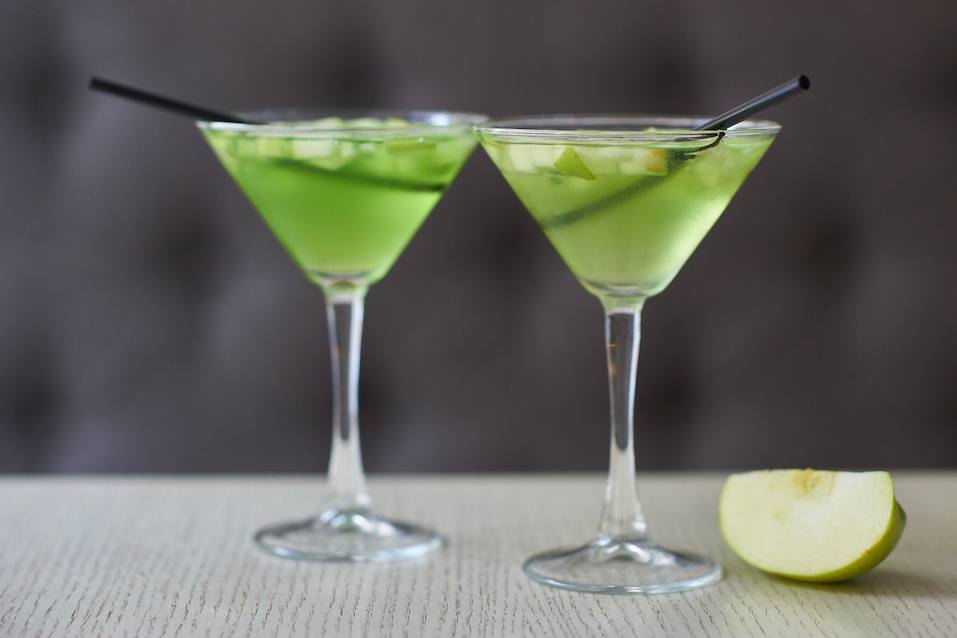 Two glasses of apple martini and apple slices on table in cafe