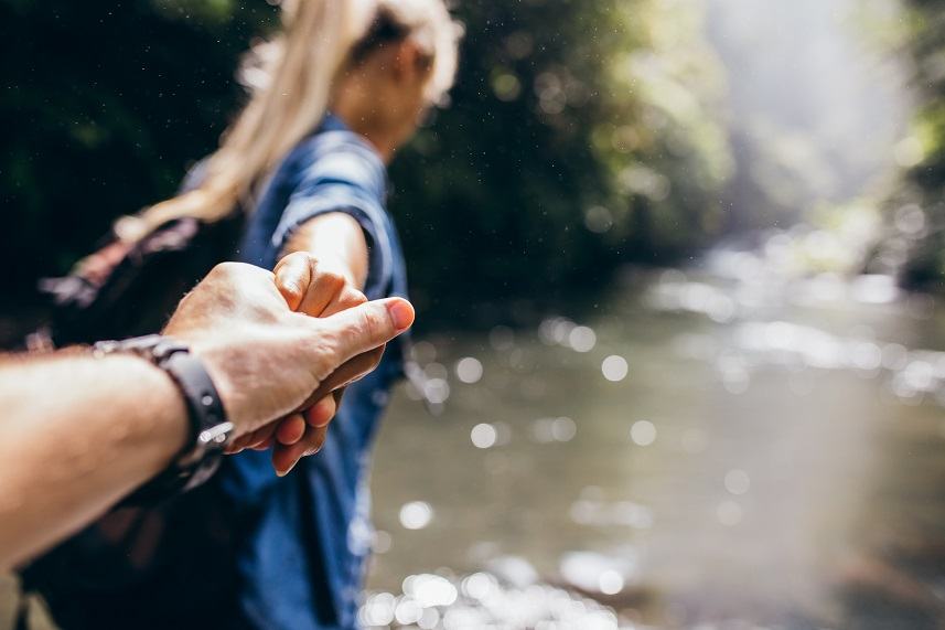 man and woman holding hands while crossing the creek