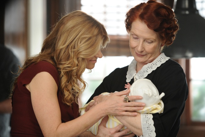 Housekeeper Moira holds an infant as mother Vivien touches and looks at him
