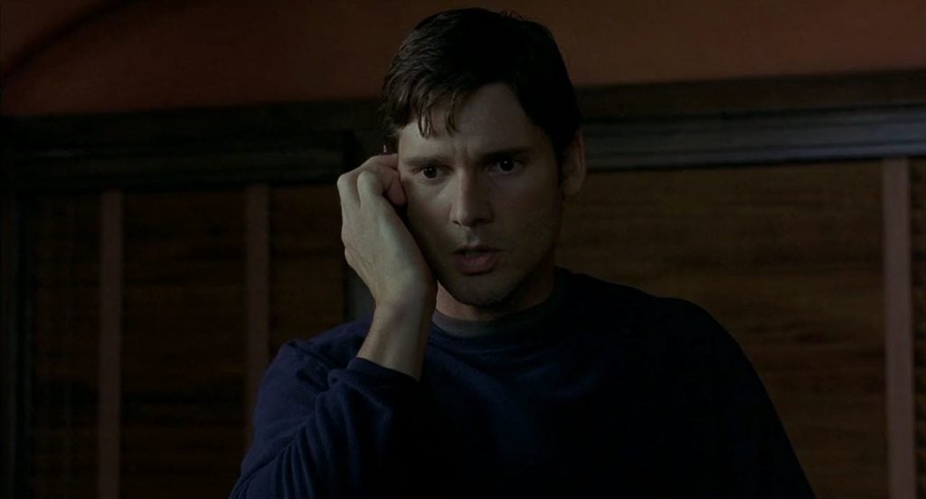 Eric Bana, holding his hand up to the right of his face, looking concerned