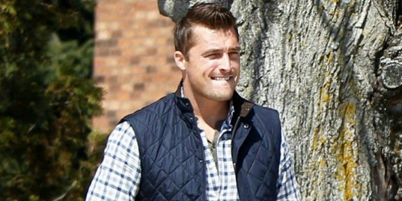 Chris Soules is biting his lip while walking near some trees.