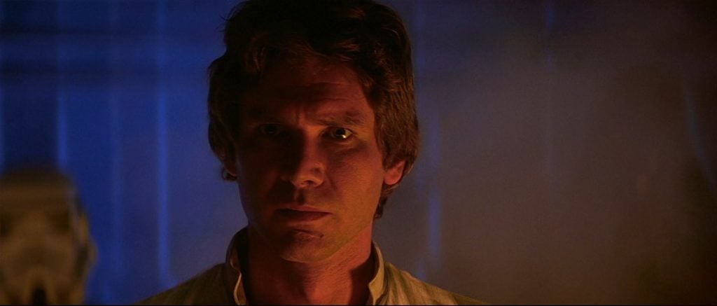Han Solo in a darkly lit chamber, looking grimly on