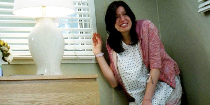 Mandy Moore is crying in a hospital gown and is in a corner of the room.