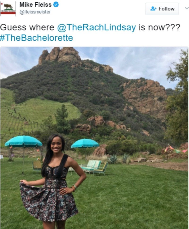 Rachel Lindsay poses in a dress in front of a beautiful green hill.