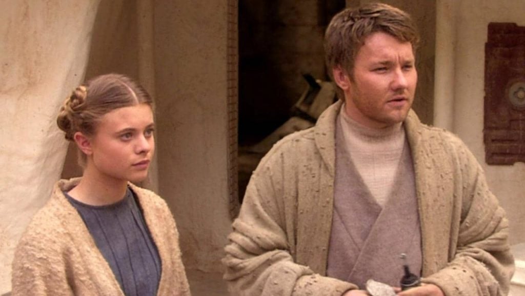 Beru and Lars wearing modest tan robes, looking off to the right of the frame bemusedly