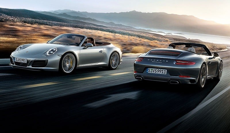 Two Porsche Carrera 911 models passing each other on a coastal highway