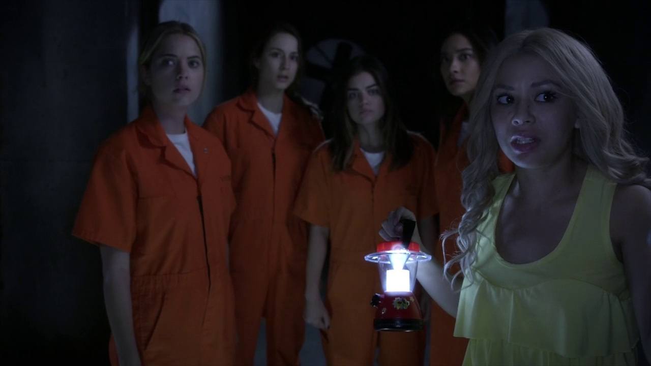 Four girls in orange jumpsuits stand behind a girl holding a lantern