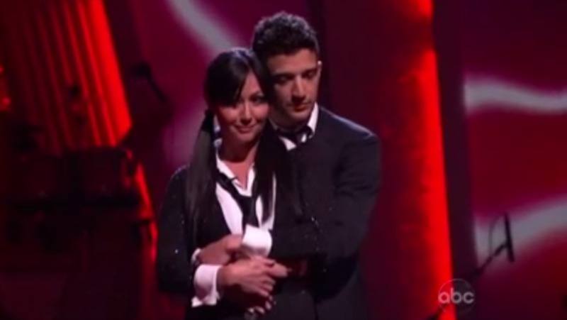 Shannen Dohert is dressed as a school girl and is being hugged by Mark Ballas.