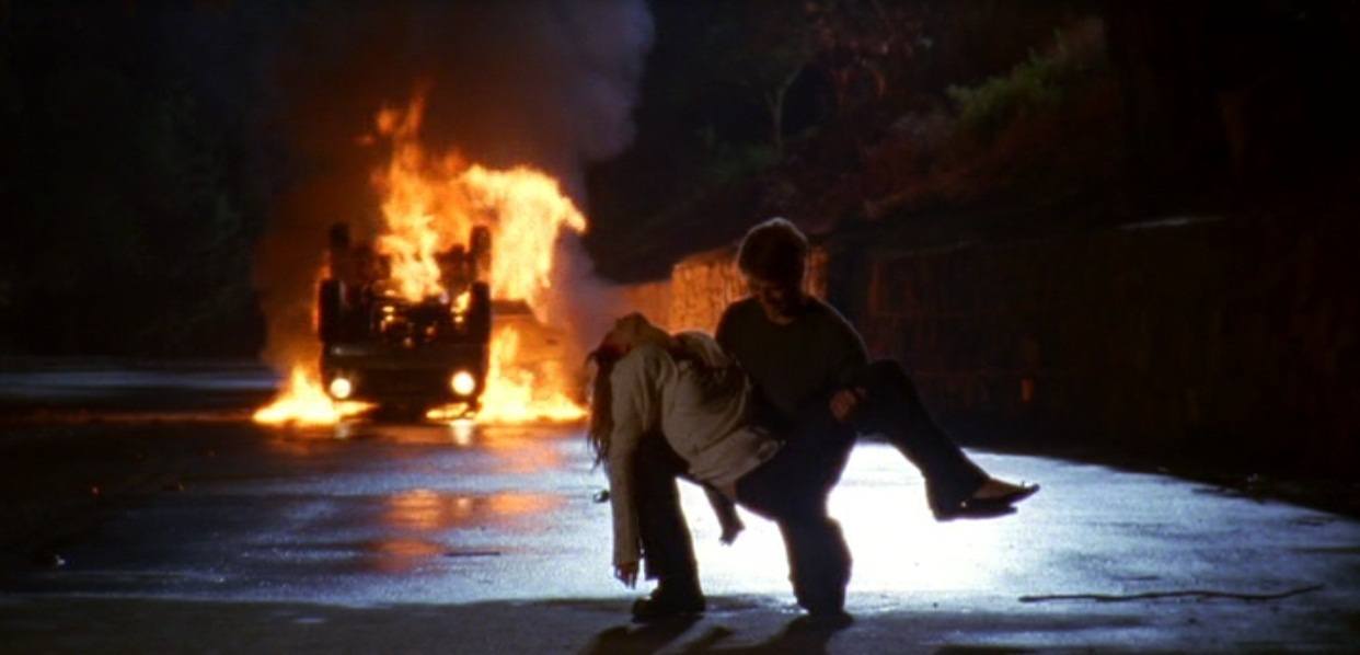 Ryan lifting Marissa off the ground while a car burns in the background