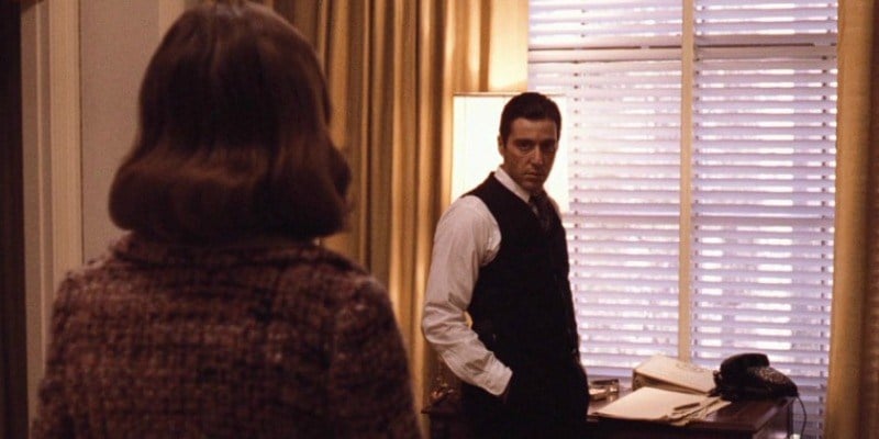 Michael Corleone looks at Kay angrily while standing by a window