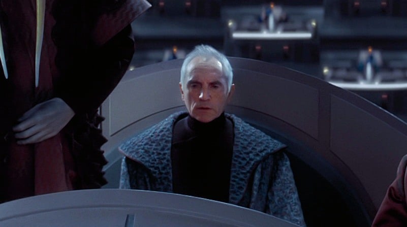 Chancellor Valorum wearing blue robes, looking off into the distance and sitting down