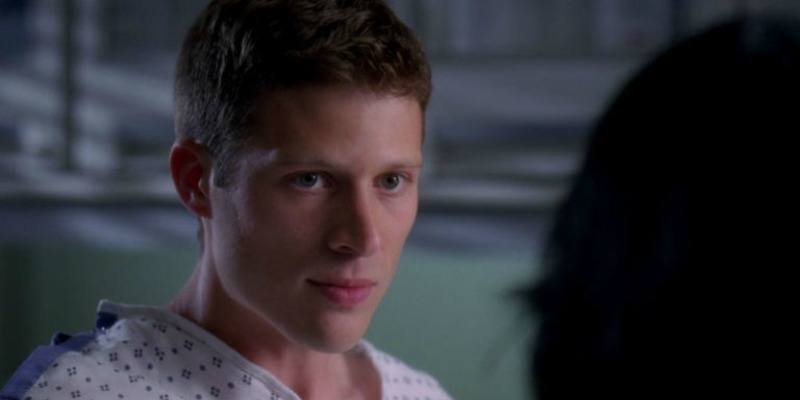 This is a closeup of Zach Gilford in a hospital gown looking at someone.