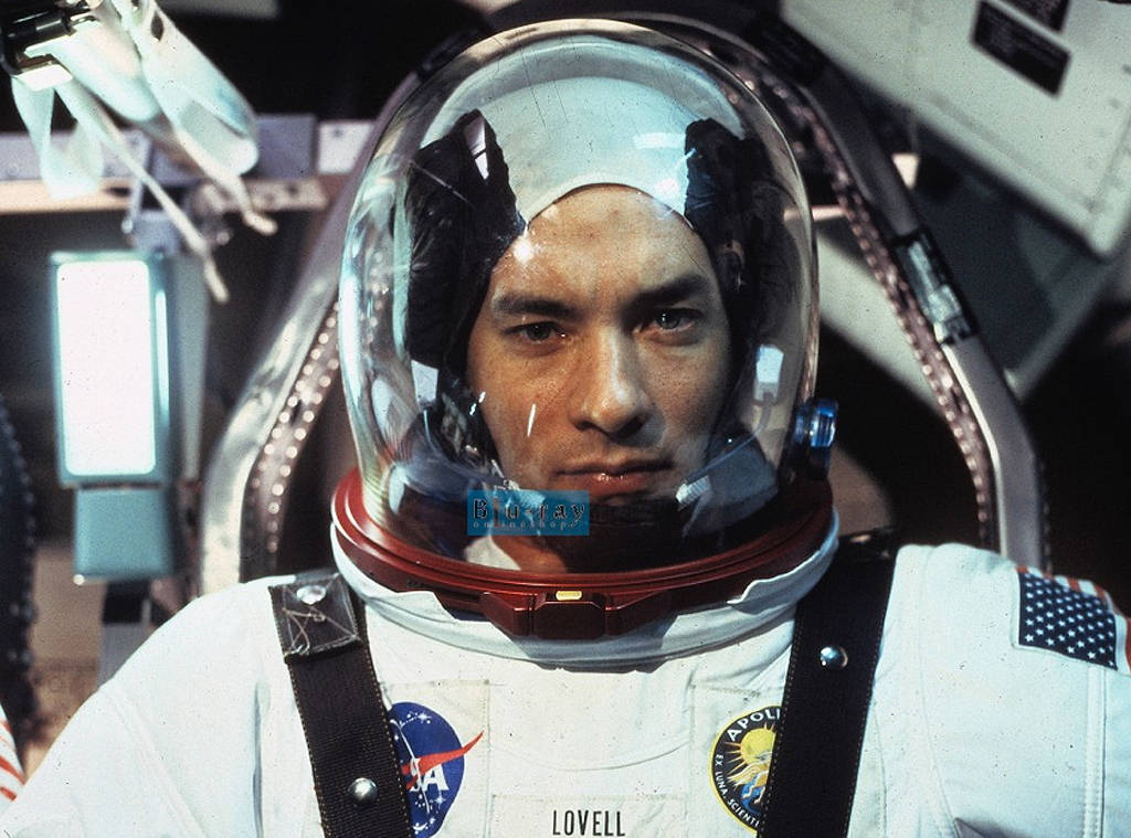 Tom Hanks wears a space suit and helmet while sitting in spacecraft in Apollo 13