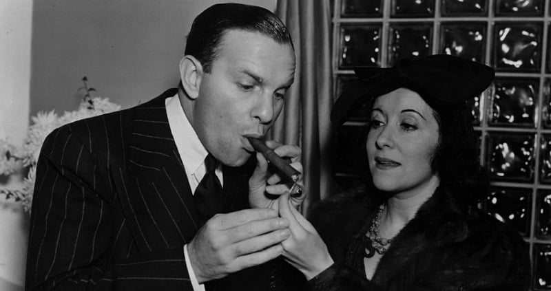 Gracie Allen is lighting a cigar for George Burns.