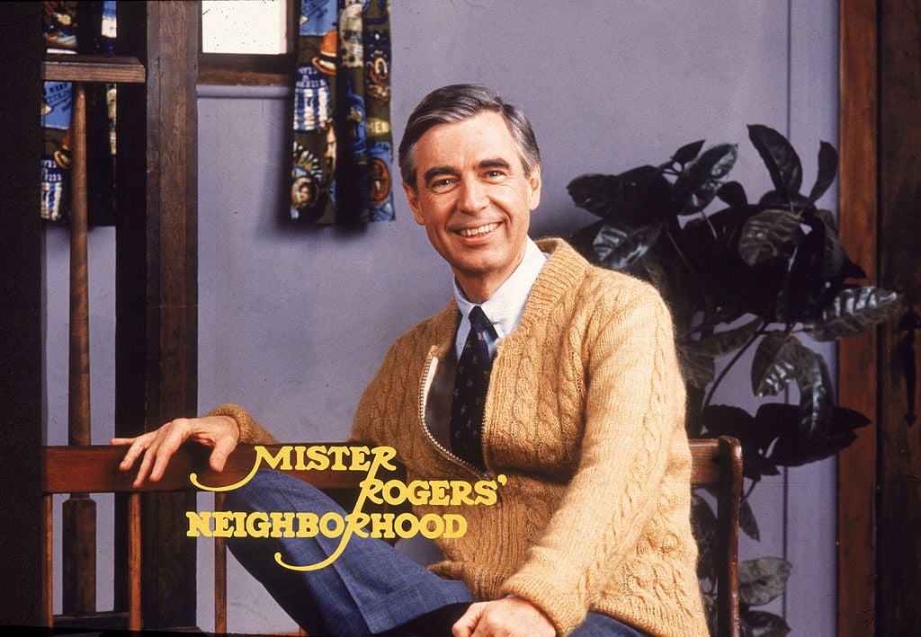 Fred Rogers sitting and posing with the words 'Mister Rogers' Neighborhood' across the image