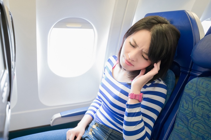 Happy young woman is sitting in the airplane, feel headache