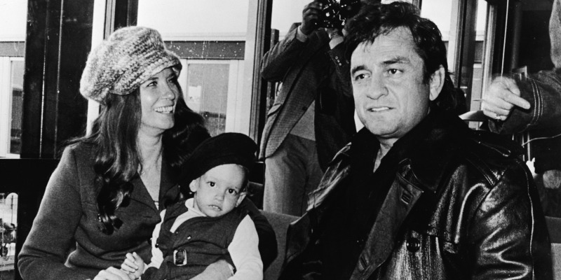 Johnny Cash and June Carter Cash are sitting next to each other. June is holding a baby.