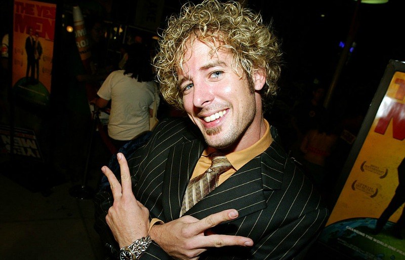 Jon Dalton is smiling and holding up two peace signs as he is wearing a striped suit.