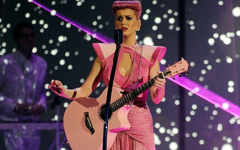 Katy Perry has pink hair and is an all-pink outfit on stage as she holds a pink guitar.