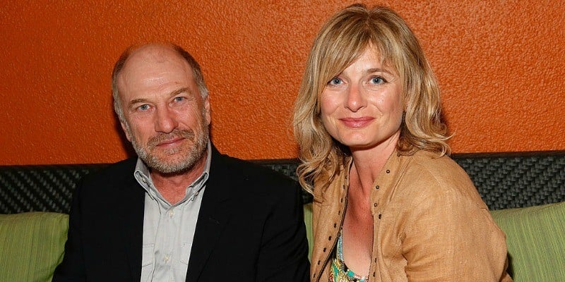 Ted Levine and his wife, Kim Phillips are sitting next to each other smiling.