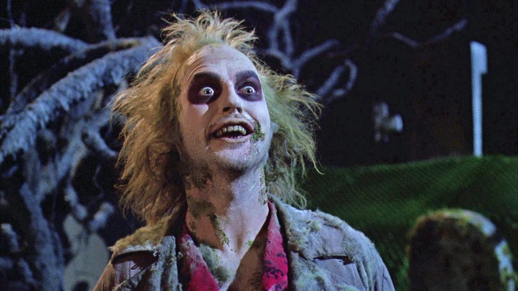 Michael Keaton as Beetlejuice, smiling maniacally and tilting his head up