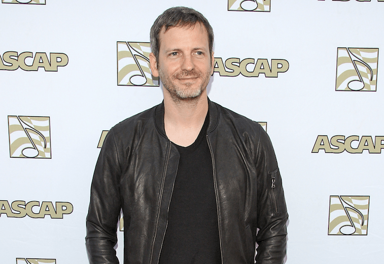 Dr. Luke poses for cameras in a black shirt and leather jacket