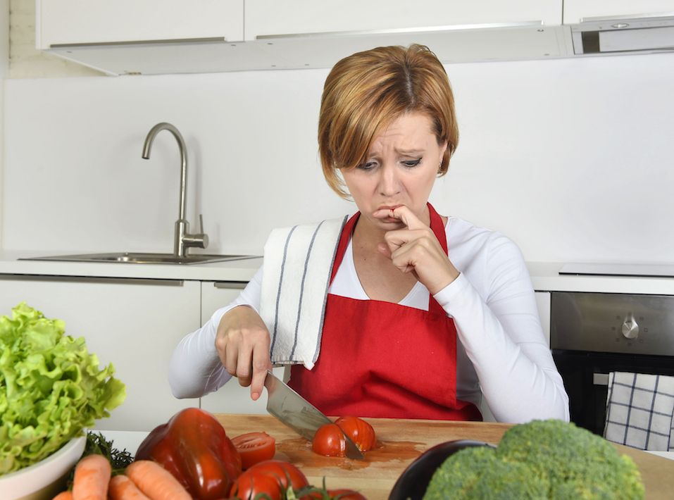 woman in red apron slicing tomato with kitchen knife suffering domestic accident cutting and hurting her finger