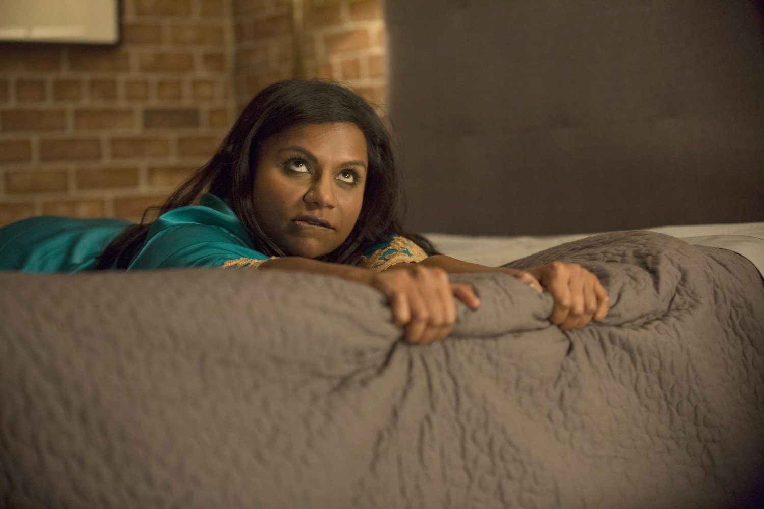 Mindy Lahiri lies on a bed gripping the side