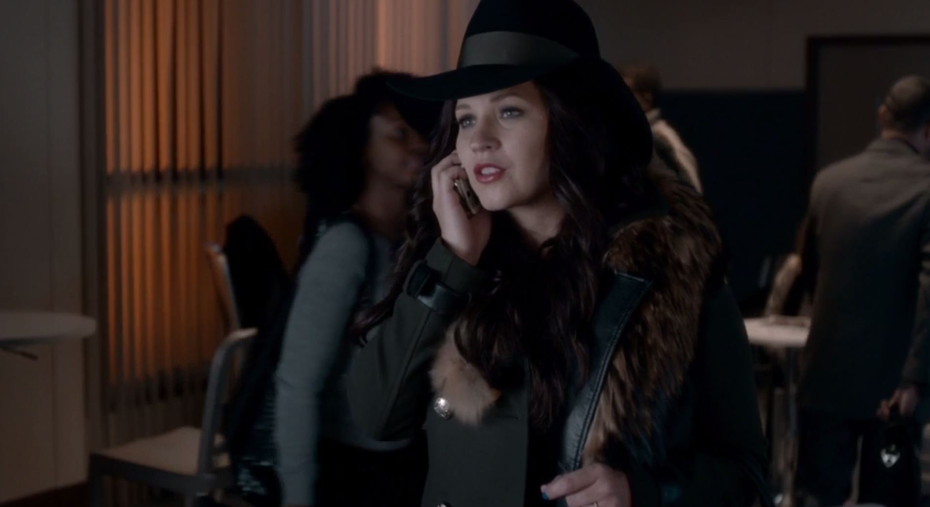 Charlotte in a brown wig and large hat talking on a cell phone