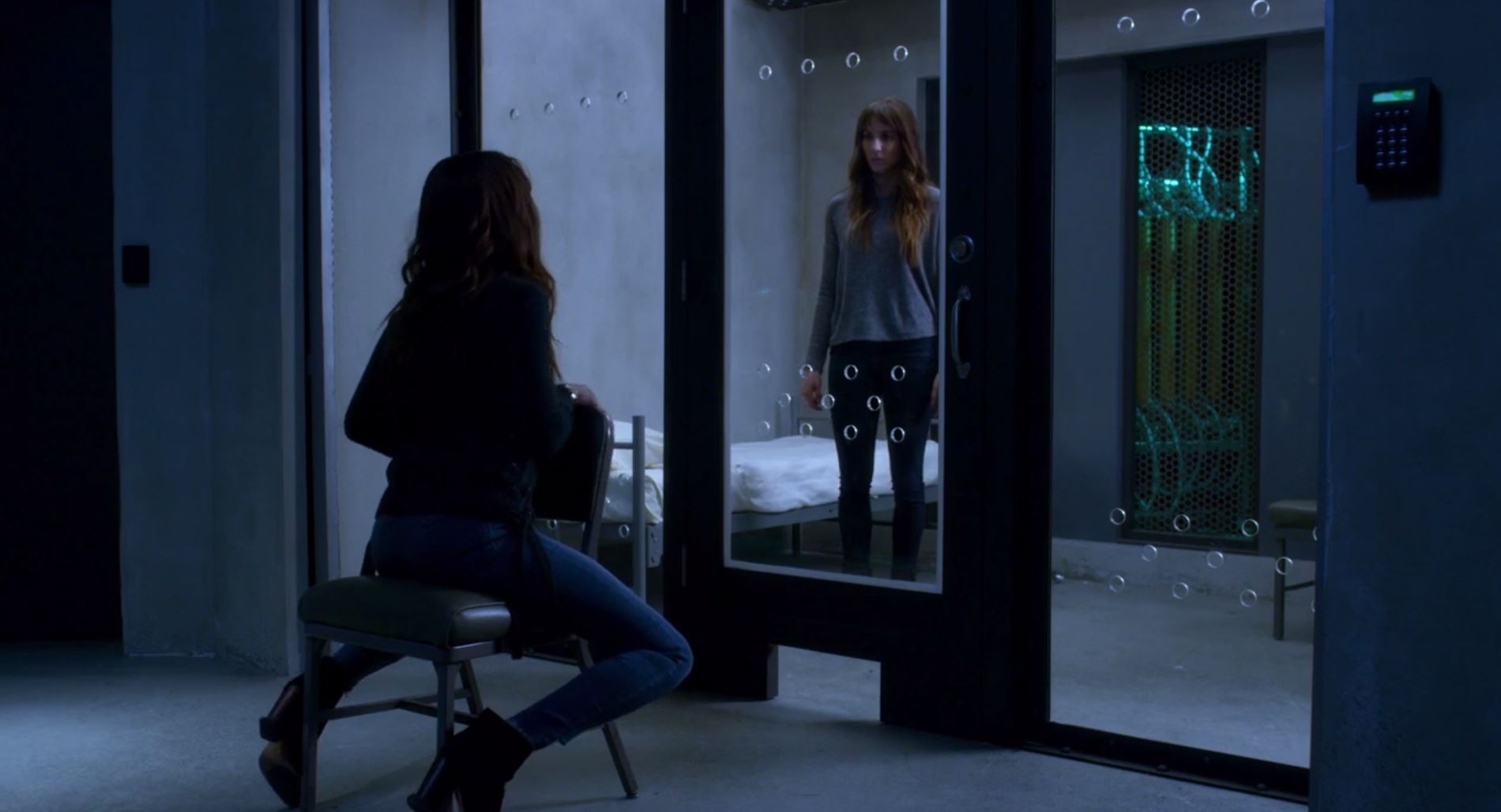 Spencer looks through a glass door at her twin sitting in a chair