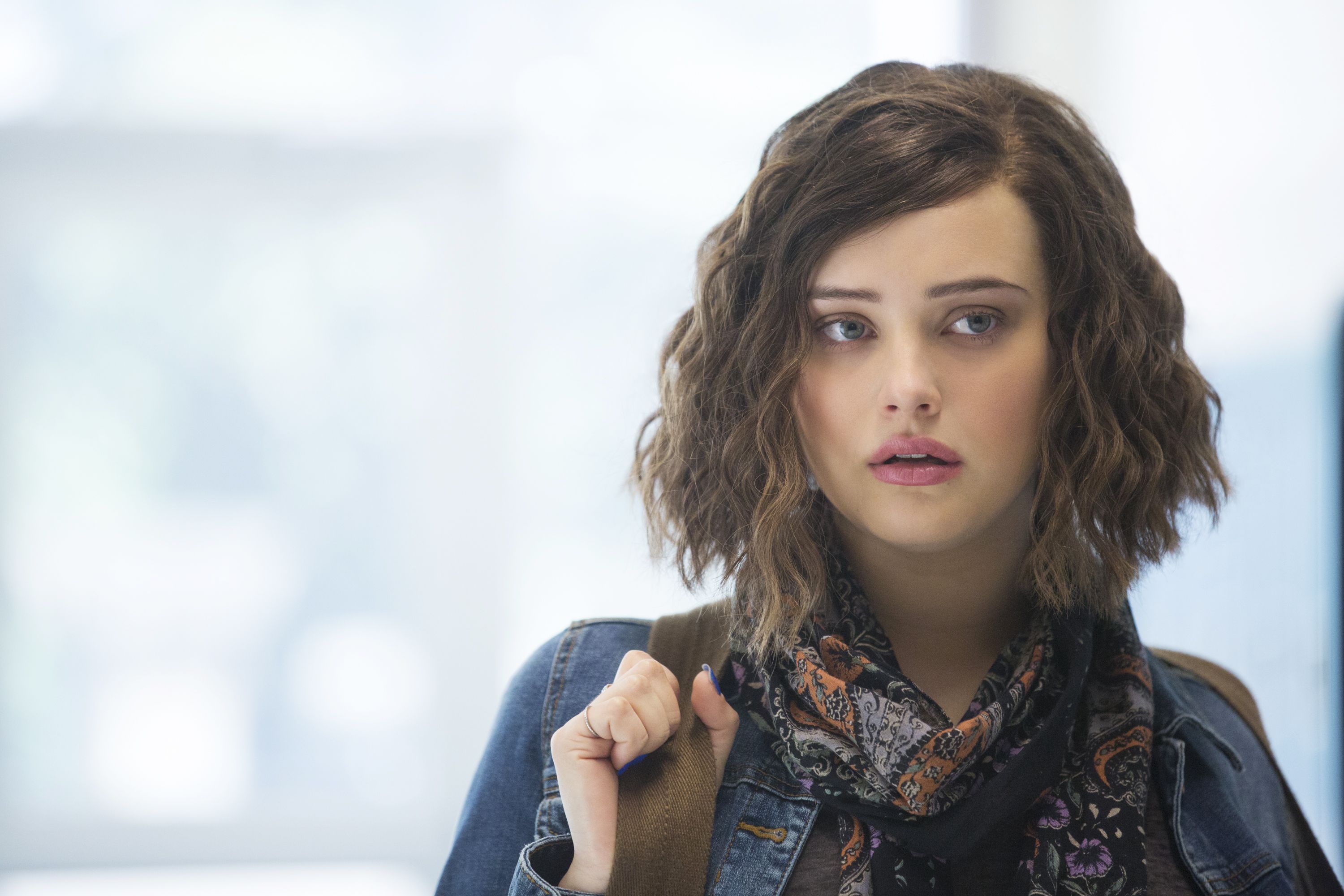 Hannah Baker holds onto the strap of her backpack while standing in a hallway
