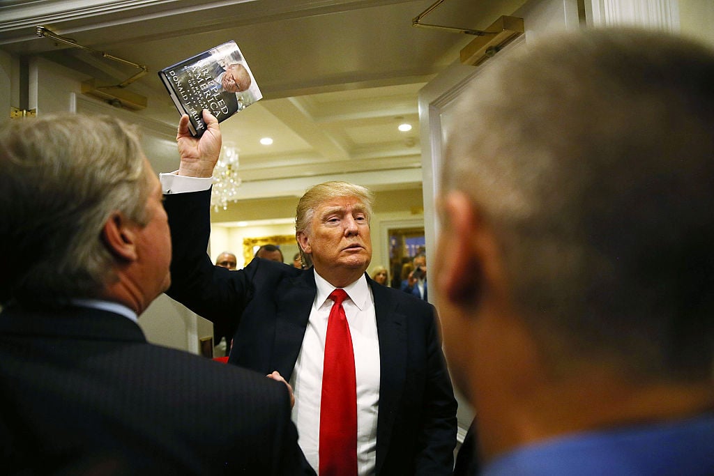Donald Trump holds up his book after holding a press conference