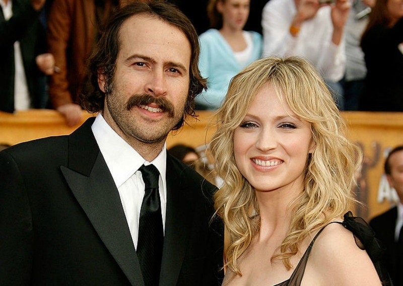 Jason Lee and Beth Riesgraf are smiling together on the red carpet.