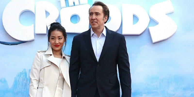 Alice Kim and Nicolas Cage pose together in front of a poster of The Croods.