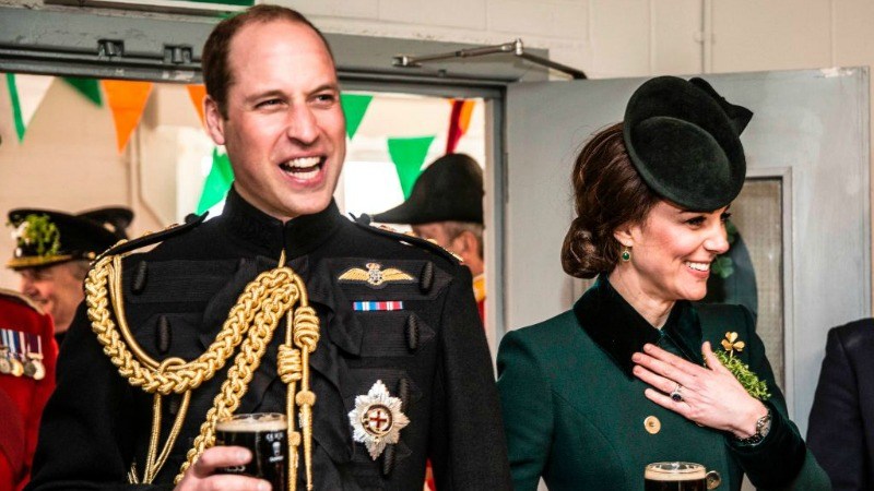 Prince William and Duchess Kate Middleton are standing next to each other holding beers and smiling.