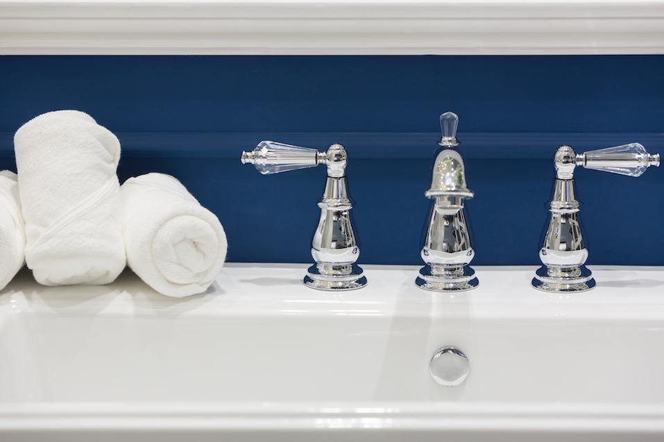 Three white hand towels on a white basin with hot and cold faucets