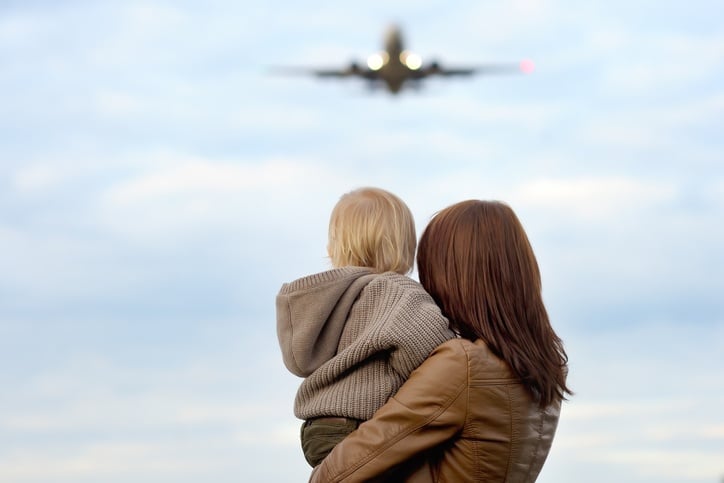 Young mother holding hes toddler son with airplane on background