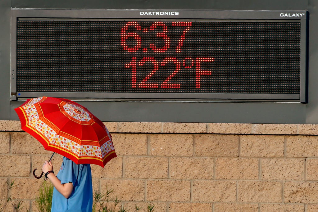 sign saying 122 degrees Fahrenheit and person holding umbrella to protect from sun in Phoenix