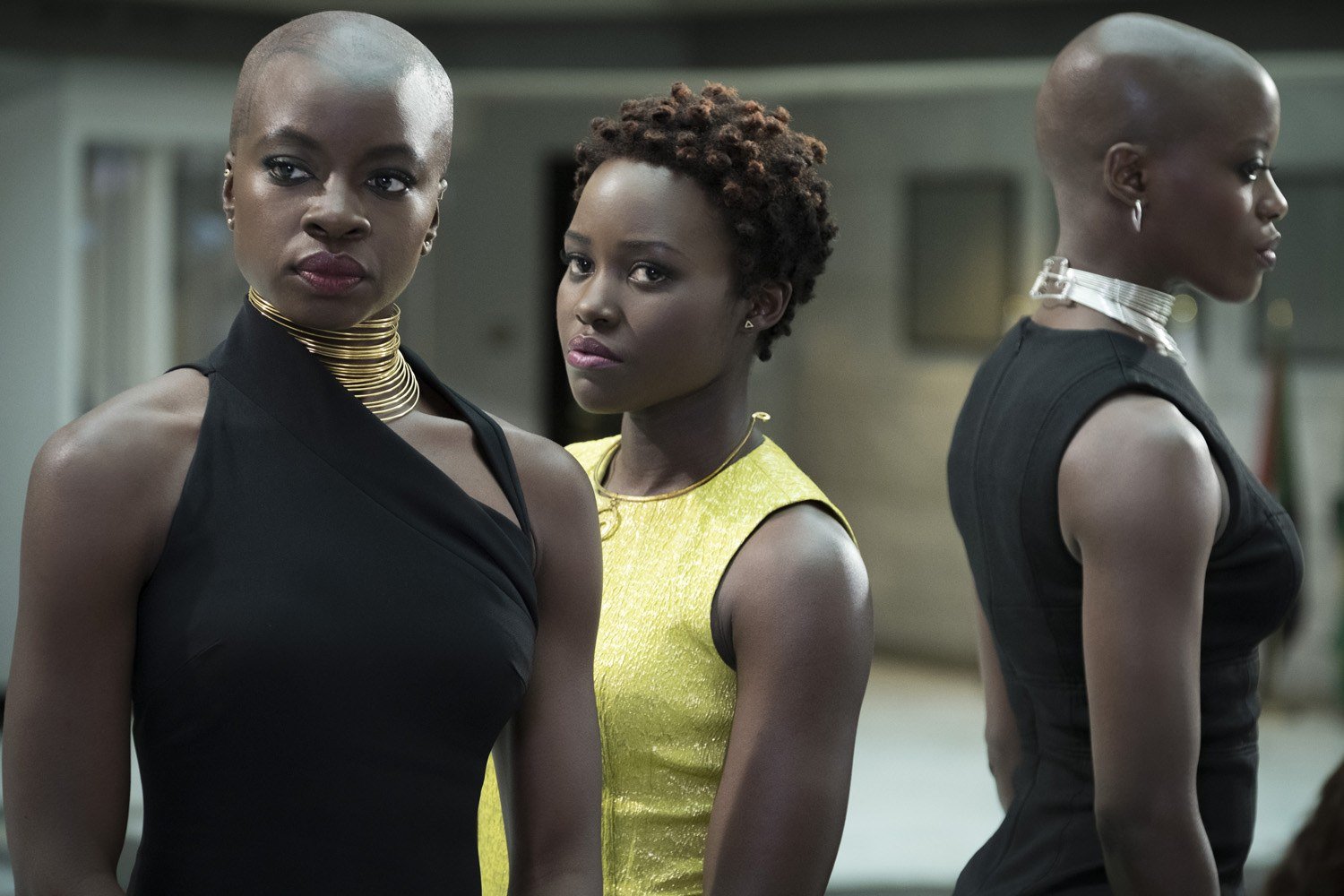 Danai Gurira's Okoye, Lupita Nyong'o's Nakia and Florence Kasumba's Ayo stand next to each other in dresses in <em>Black Panther</em